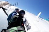 Two skydivers in helmets and jumpsuits prepare to jump from an airplane. They are holding onto the side of the aircraft, which has "Skydiving Center" written on it, with a clear blue sky in the background.