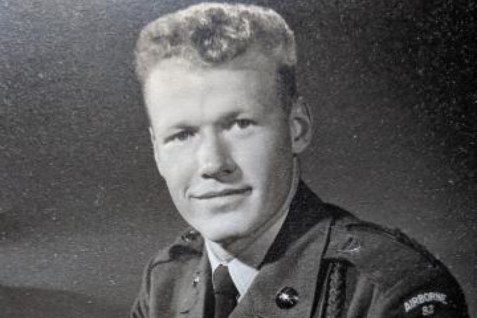 Black and white photo of a man in military uniform with a patch on his shoulder. He has short hair and is facing forward, looking at the camera.