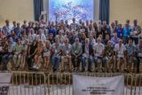 A large group photo of people, mostly men and a few women, standing and sitting on risers indoors. They are smiling and dressed in casual to semi-formal attire. A banner reads "World Team 2006—400+ Way Largest Formation World Record.