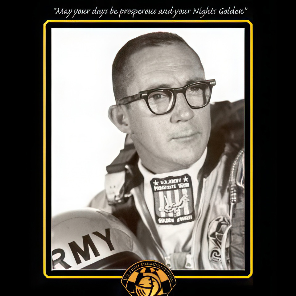 Pilot wearing glasses and an aviation suit with various patches stands holding a military helmet labeled "ARMY." A quote above reads, "May your days be prosperous and your nights golden." A logo is at the bottom. Black and white photo.