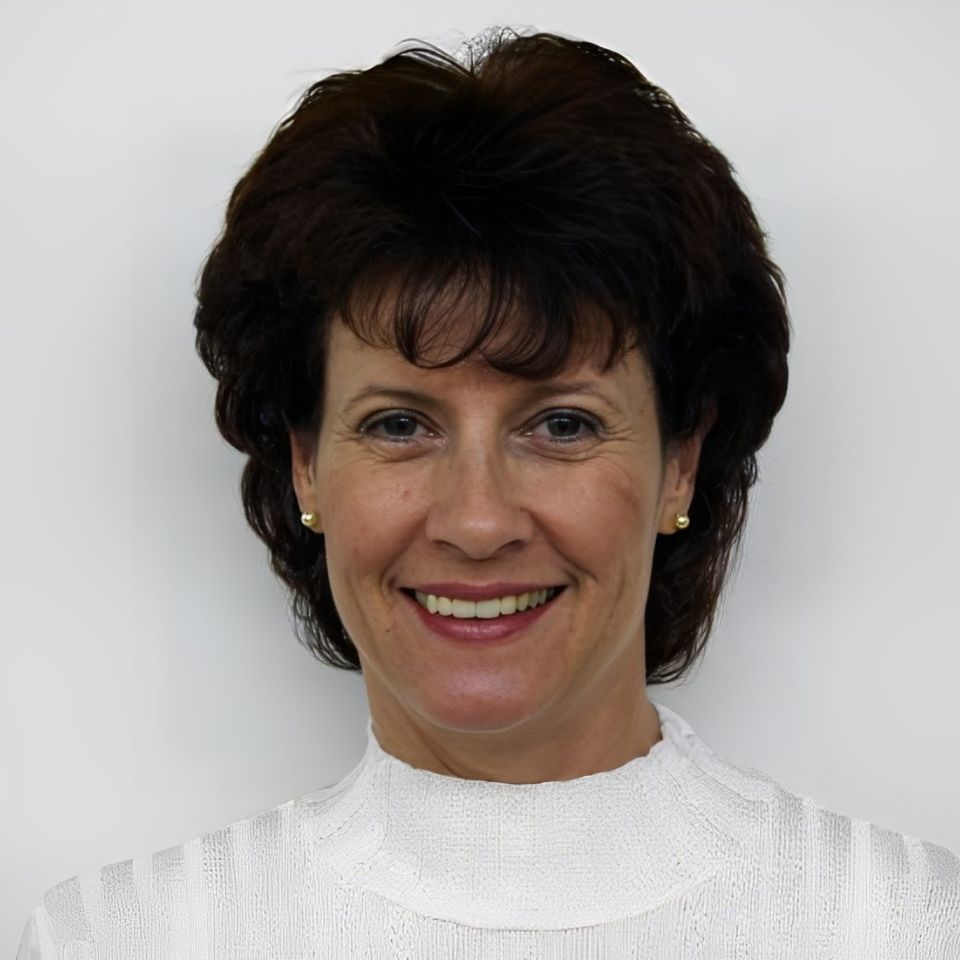 Smiling woman with short, dark hair wearing a white turtleneck sweater against a plain background.