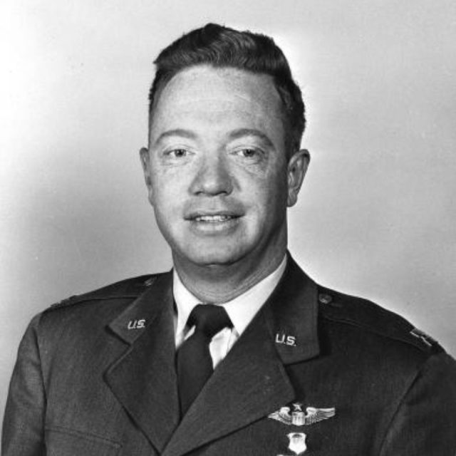 A man in a military uniform, featuring U.S. Air Force insignia, poses for a portrait against a plain background. He has short hair and is smiling slightly.