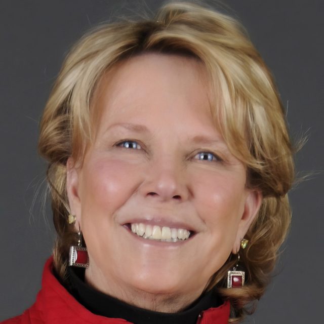 Smiling woman with short, wavy blonde hair, wearing a red jacket and red square earrings, set against a gray background.