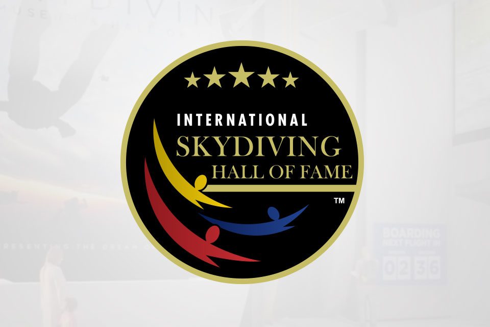 Logo of the International Skydiving Hall of Fame. It features a circular design with three stylized skydivers in red, yellow, and blue, and five stars across the top of the black background.