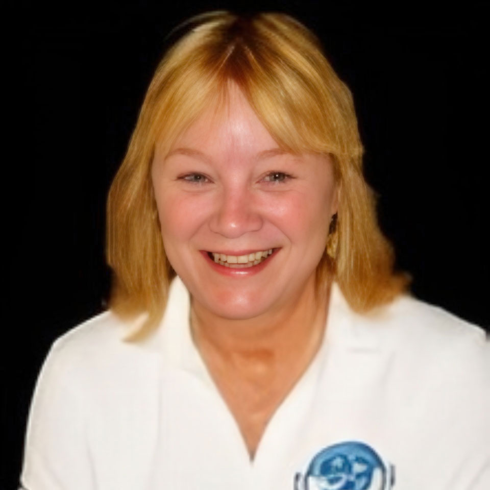 A smiling woman with blonde hair wears a white shirt with a blue and white logo on it. The background is black.