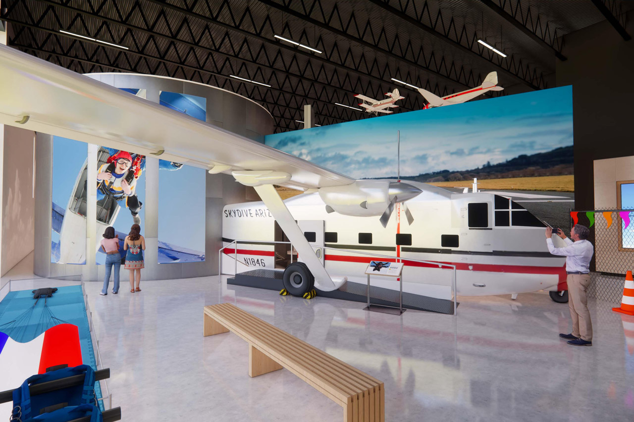 Interior of an aviation-themed hall with a large skydiving aircraft for people to walk through. An individual is observing and taking a photo.